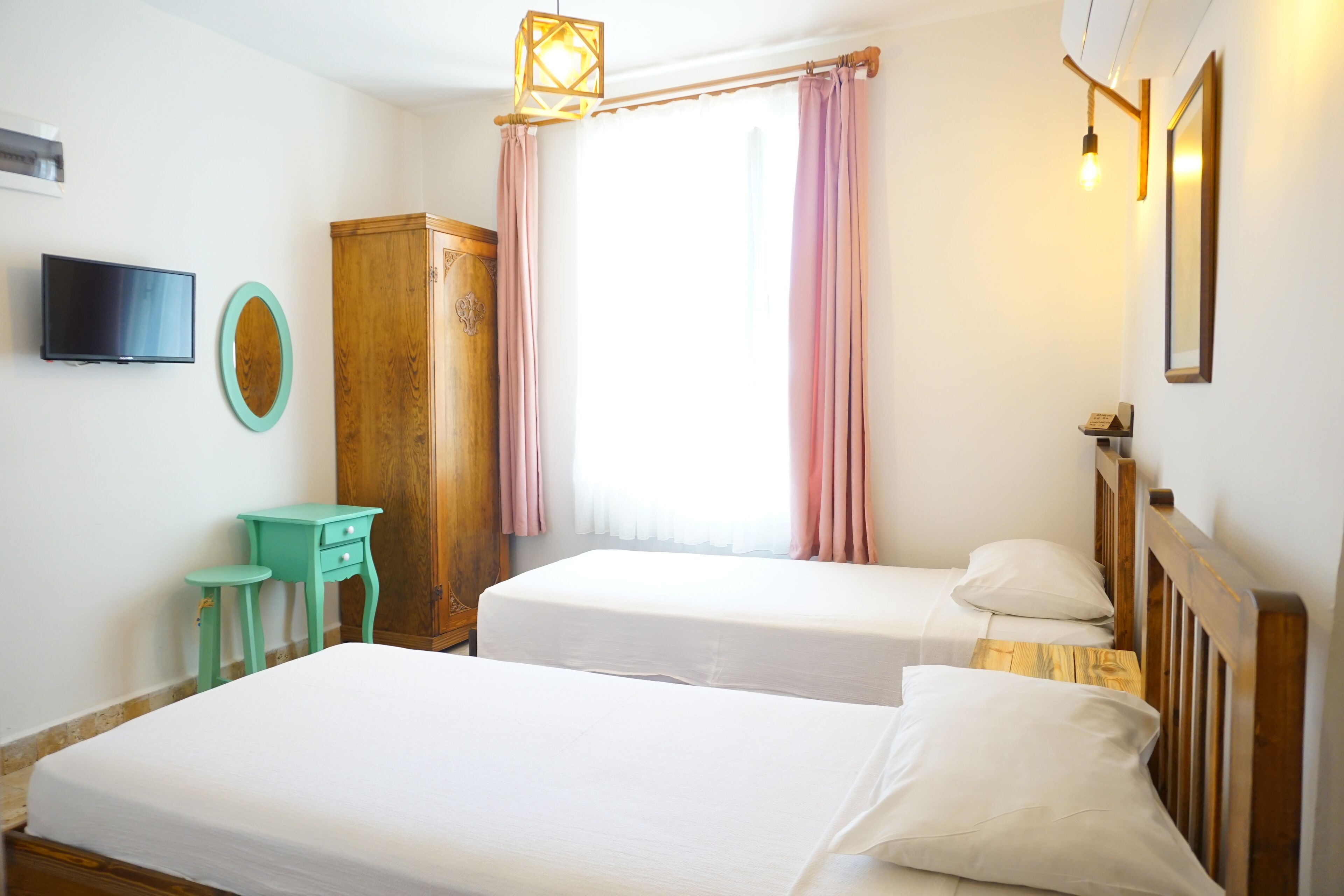A room with two beds, a TV, a wooden wardrobe, and a small stool.