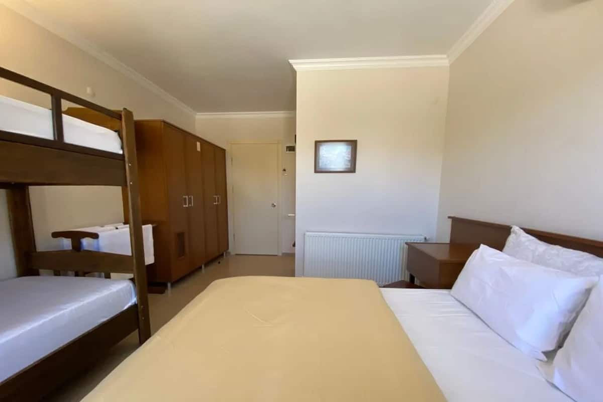 Ein Zimmer mit einem Etagenbett, einem Einzelbett, Holzschränken, einem Heizkörper und einem gerahmten Bild an der Wand.
