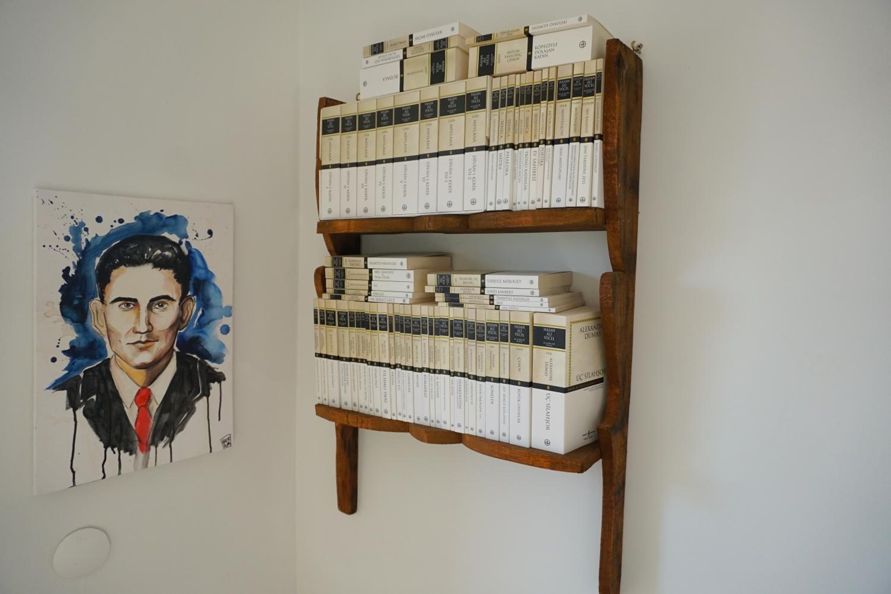 Una estantería con varios libros y un cuadro en la pared.