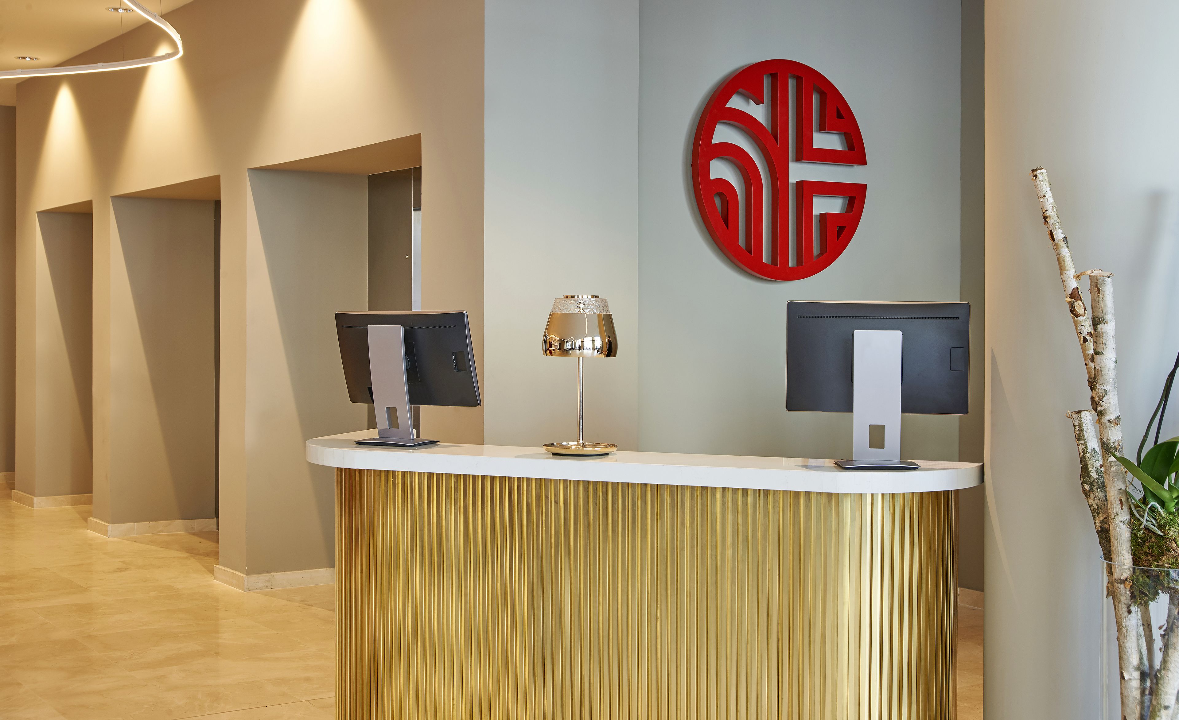 A reception desk with two monitors, a lamp, and a decorative wall piece.