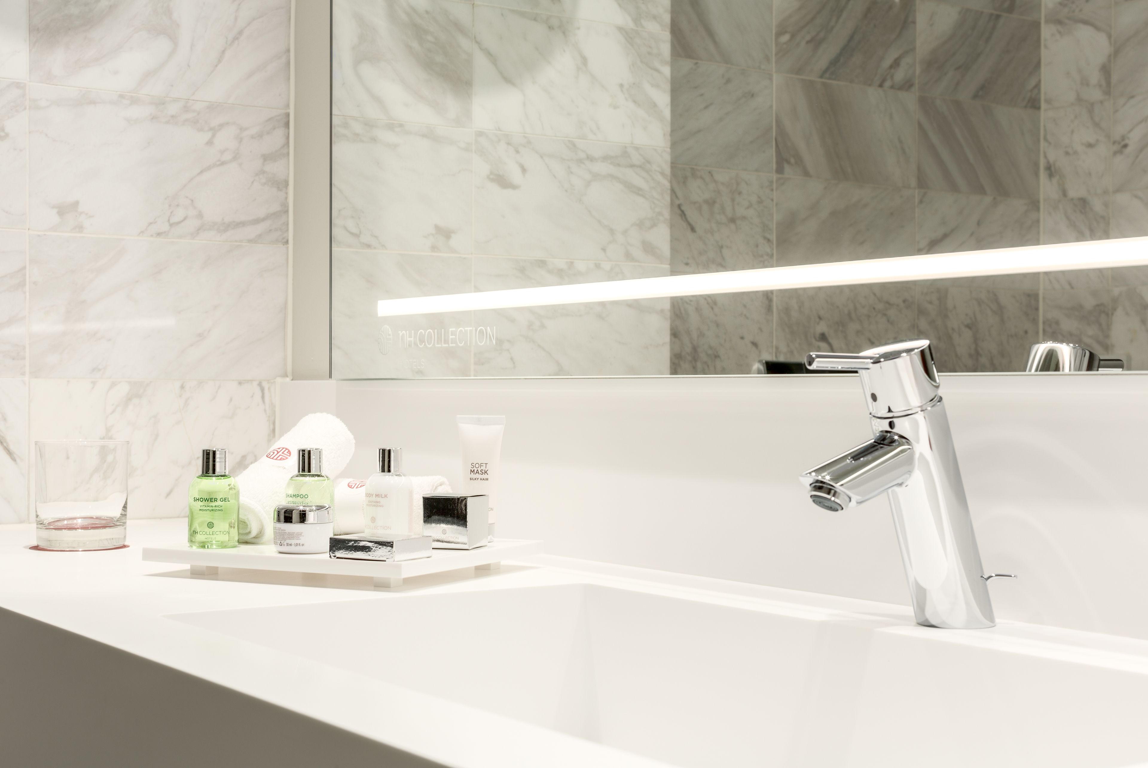 Une salle de bain moderne avec un pare-baignoire en marbre, un grand miroir et un robinet chromé.