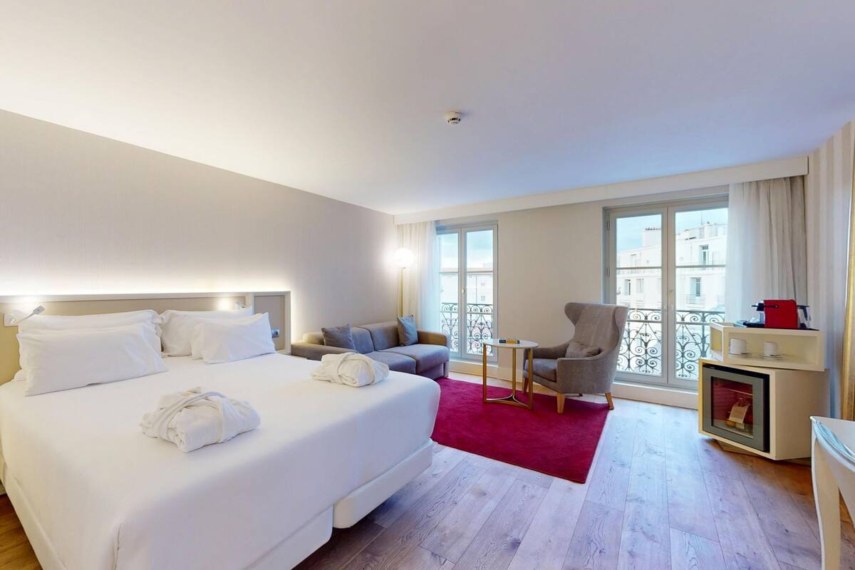 Une chambre d’hôtel avec un grand lit, un canapé, une petite table, une chaise et un balcon doté d’une balustrade.