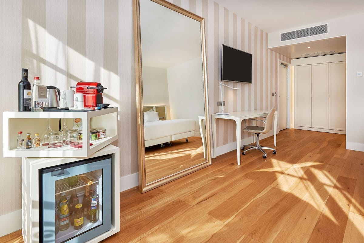 Une chambre d’hôtel avec un plancher en bois, un lit, un bureau, une télévision, une armoire et un mini-bar.