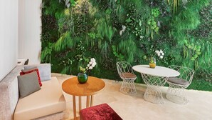 Una sala de estar moderna con una pared de musgo verde, una mesa redonda de madera, sillas blancas de estructura metálica y un sofá color beige con cojines.