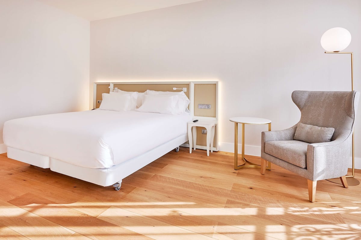 Une chambre d’hôtel moderne avec un grand lit, une table de chevet, une chaise et une lampe sur pied.