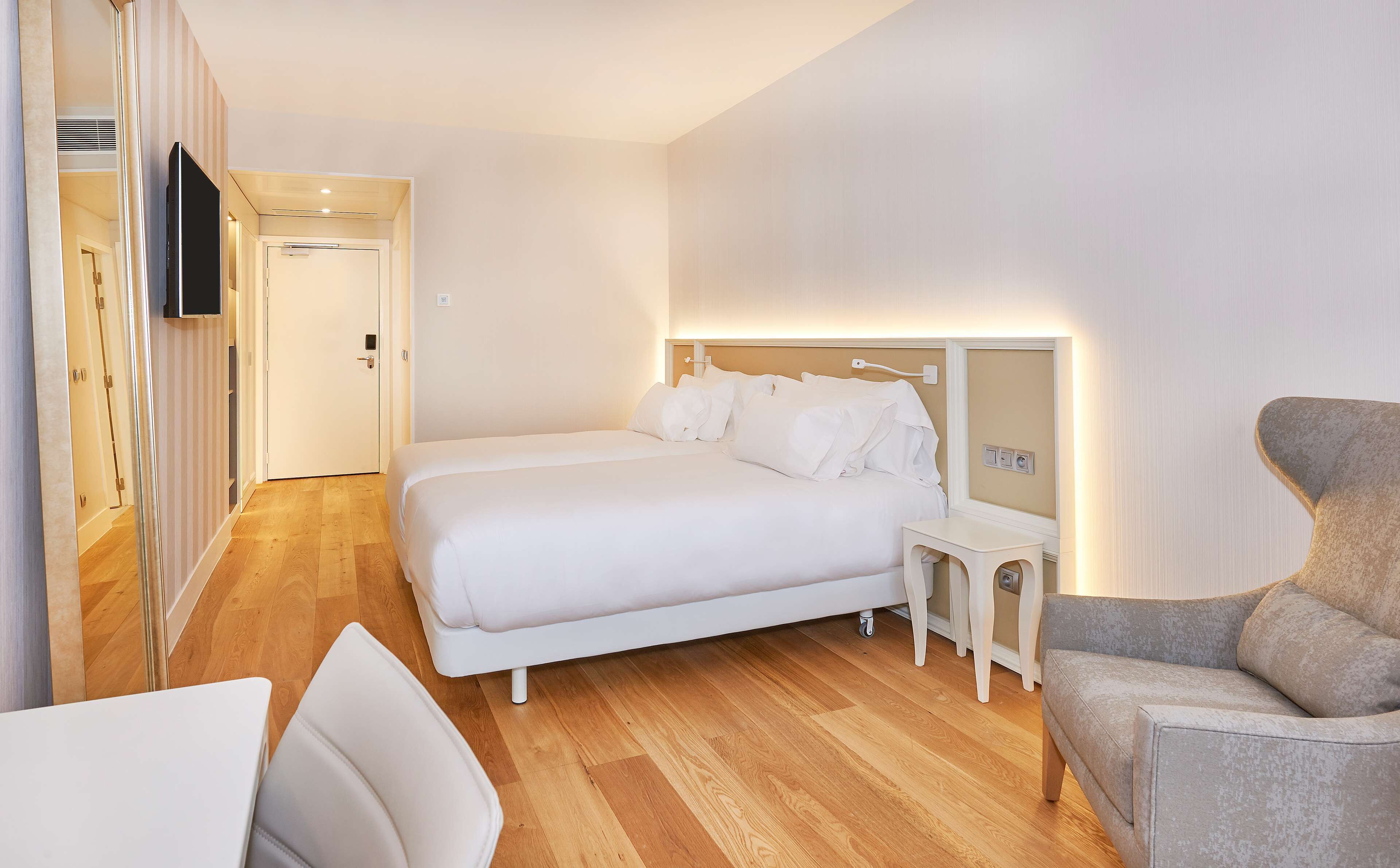 A hotel room with a bed, bedside table, chair, and a TV mounted on the wall.