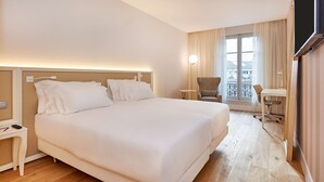 Habitación de hotel con una cama grande, un escritorio, una silla y un balcón con cortinas.