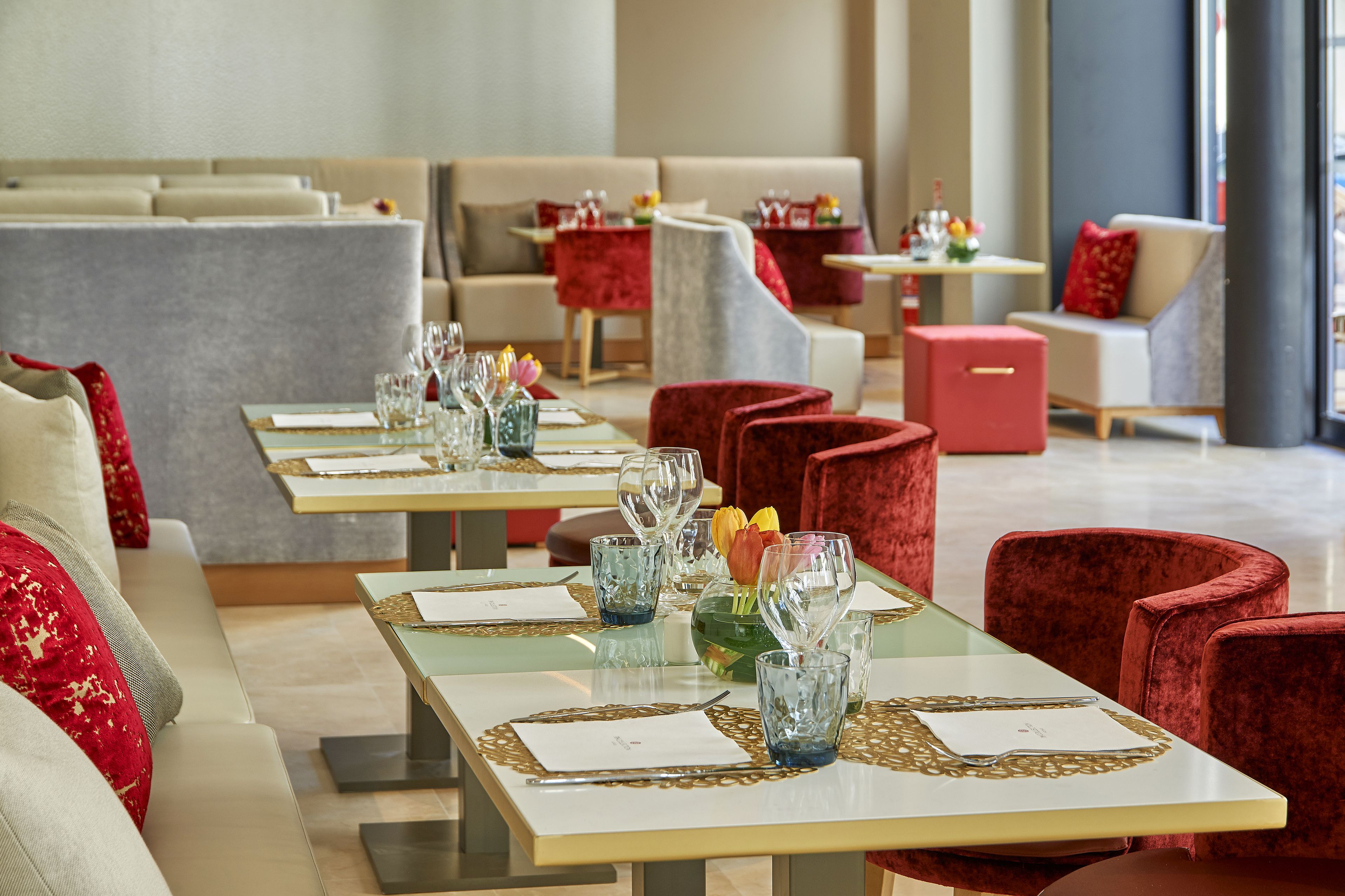 Un restaurante con varias mesas dispuestas para comer, con sillas tapizadas rojas y una decoración interior moderna.