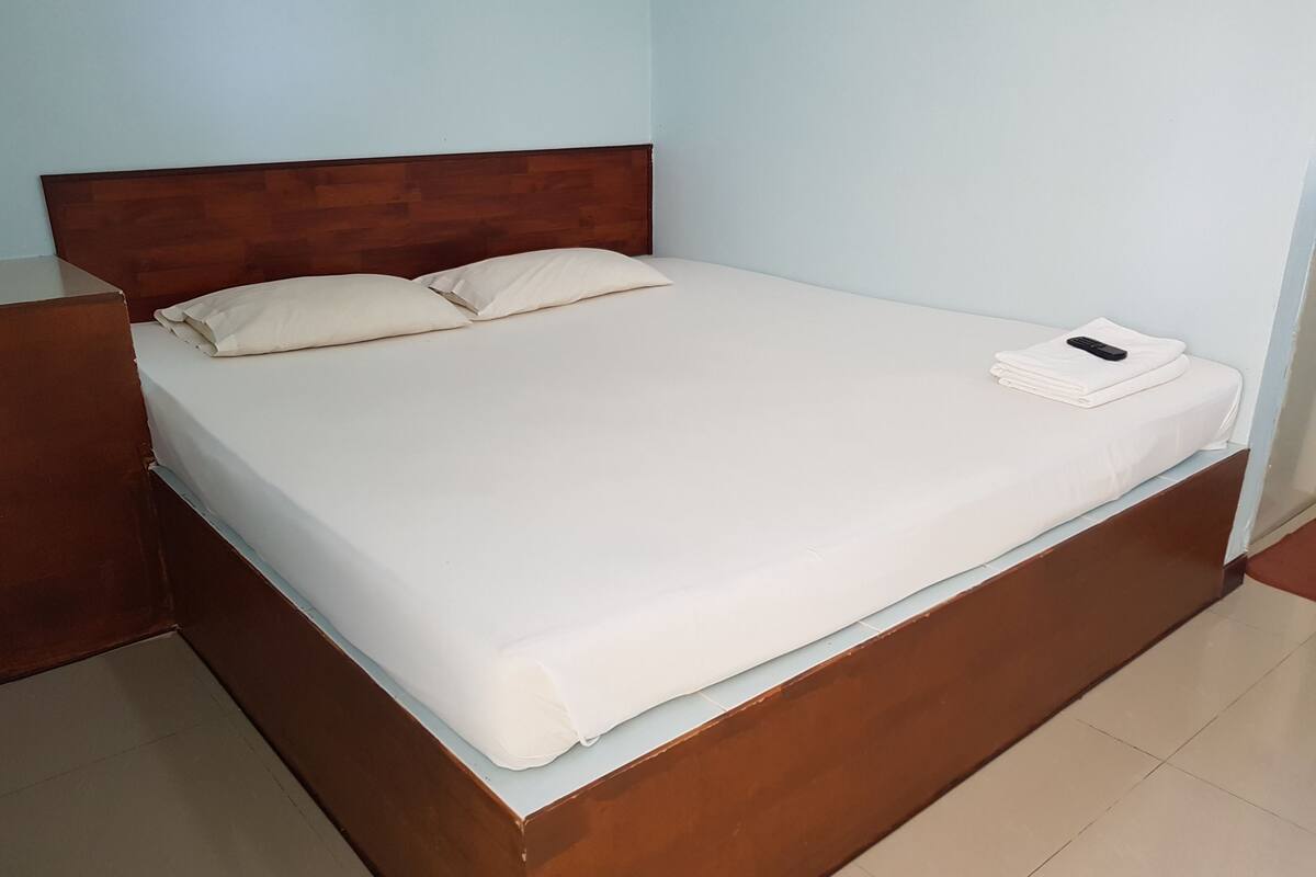 A neatly made bed with a wooden headboard, a white mattress, and a folded white towel on the footboard.
