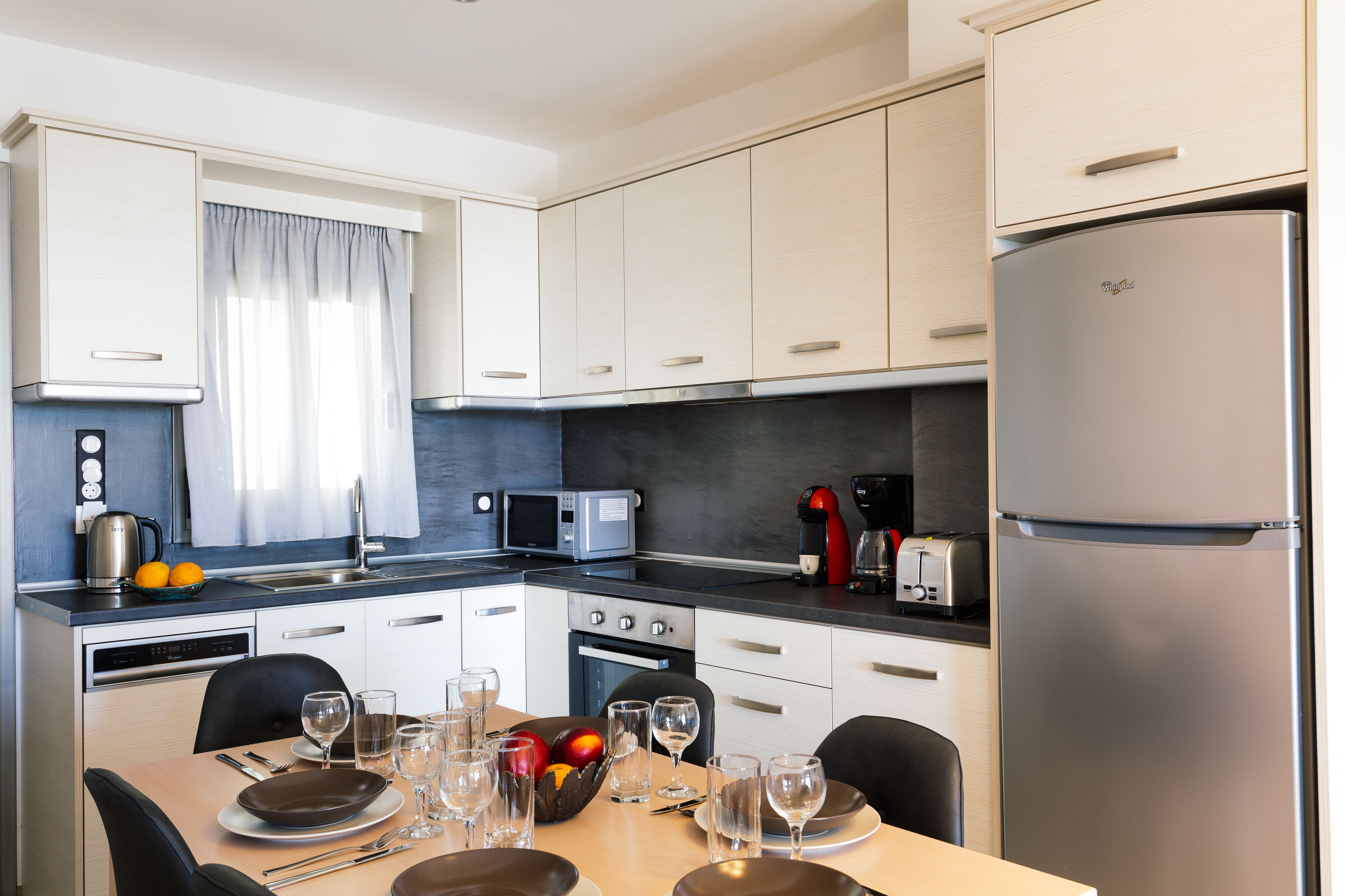 A modern kitchen with white cabinets, a stainless steel refrigerator, a microwave, and a coffee maker.