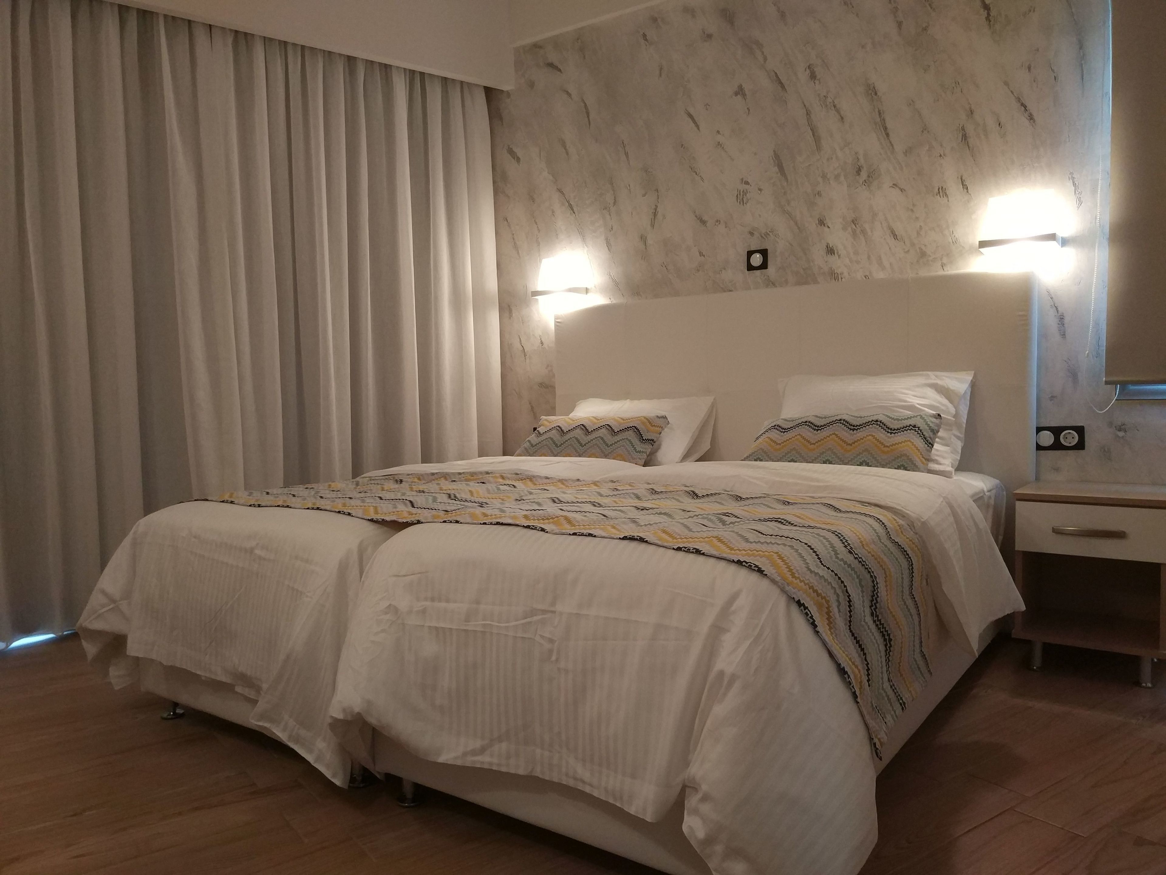 Une chambre bien rangée, avec un grand lit, une table de chevet et un luminaire fixé au mur.