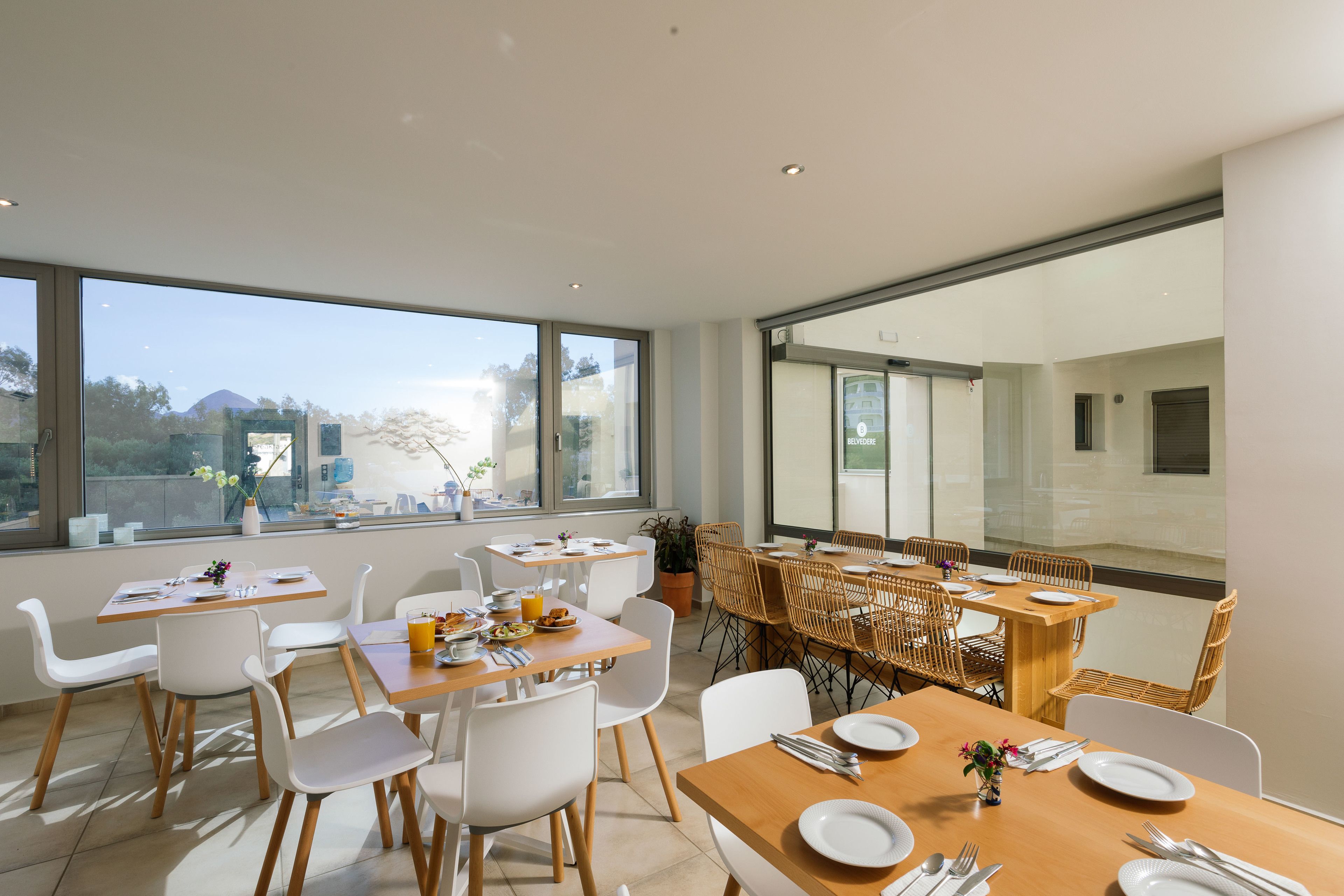 Un comedor moderno con ventanas amplias, sillas blancas, mesas de madera y vistas a la montaña.