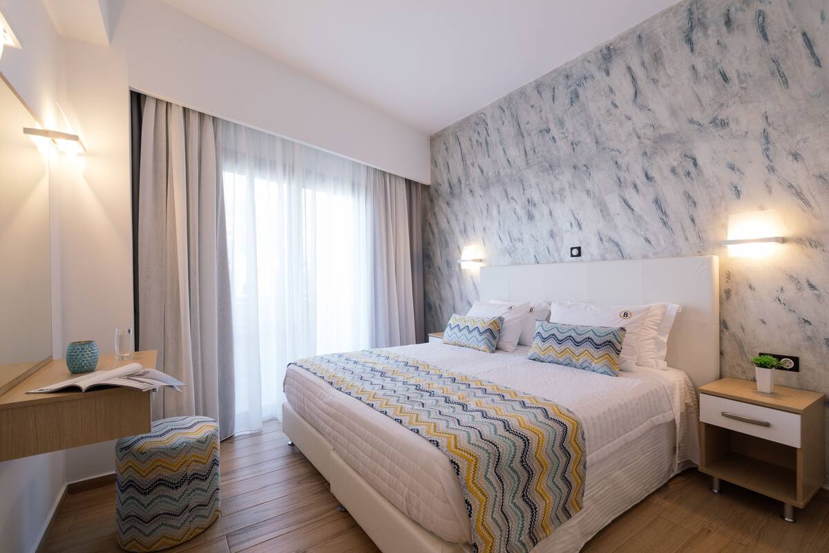 A modern bedroom with a large bed, a nightstand, a bedside table, and a window with curtains.