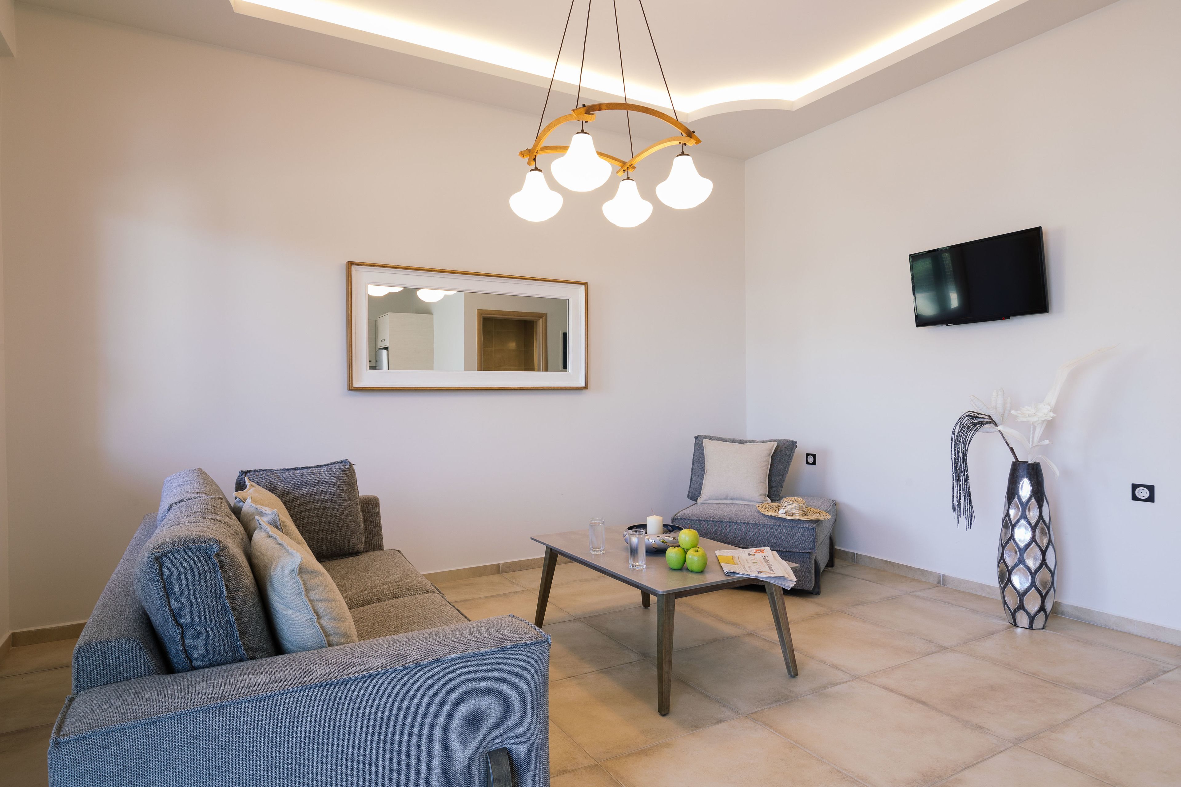 Een moderne woonkamer met een bank, een bijzettafeltje met appels en een kaars, een aan de muur bevestigde televisie en een decoratieve vaas.