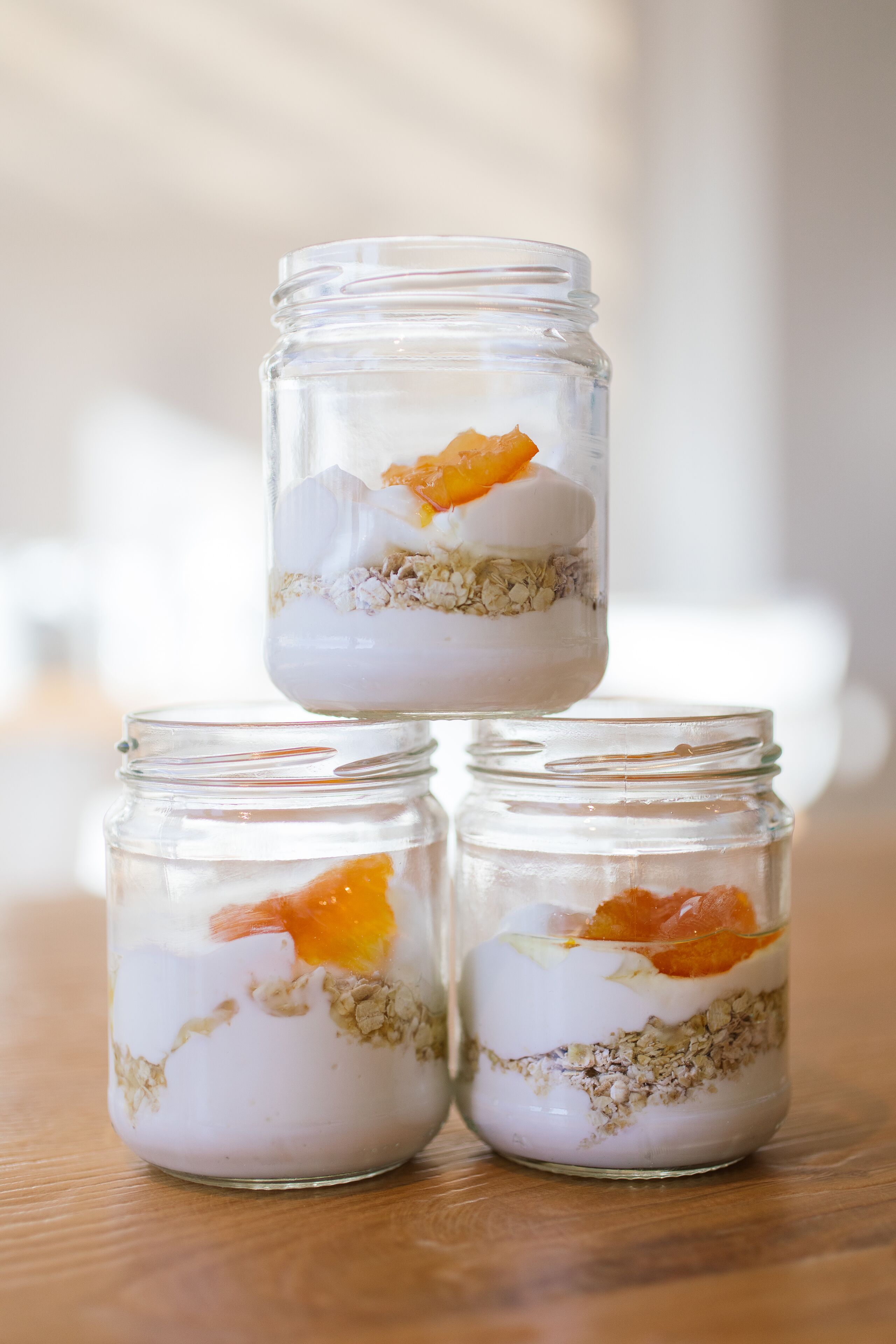 Tres frascos de vidrio con capas de contenido, que parecen ser yogur, granola y rodajas de naranja, sobre una superficie de madera.