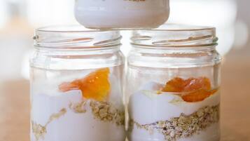 Tres frascos de vidrio con capas de contenido, que parecen ser yogur, granola y rodajas de naranja, sobre una superficie de madera.