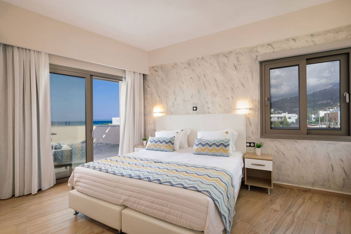 A bedroom with a large bed, a nightstand, a window with a view, and a balcony.