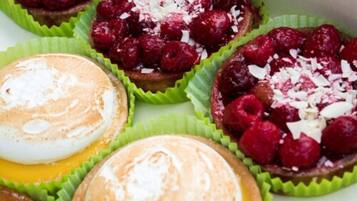 Une variété de pâtisseries présentées dans des caissettes en papier vert, dont une garnie de framboises et de copeaux de noix de coco.