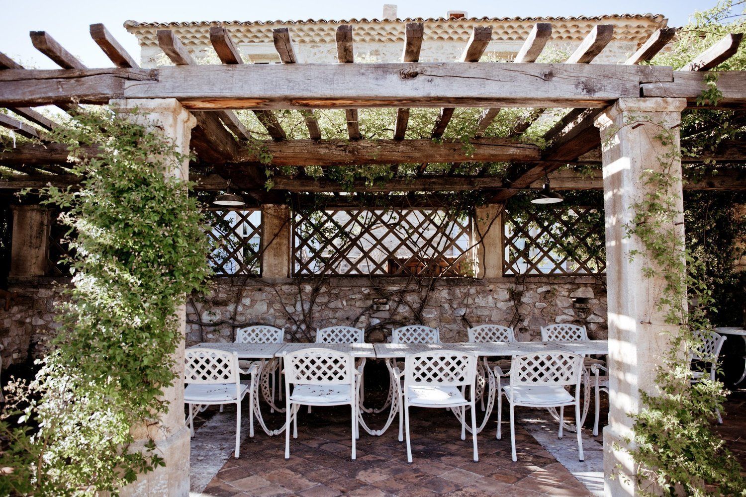 A covered outdoor seating area with stone walls and white lattice chairs.