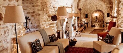 A cozy, stone-walled interior with a sofa, armchairs, and a red carpet.