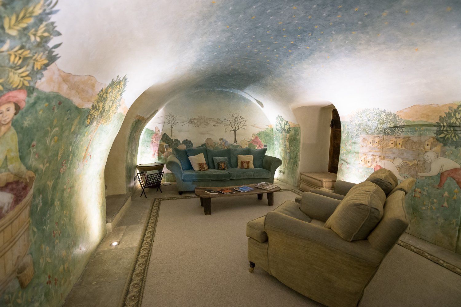 Una sala de estar acogedora y semicircular, con un mural en las paredes, un sofá azul, un sillón marrón y una mesa de centro.