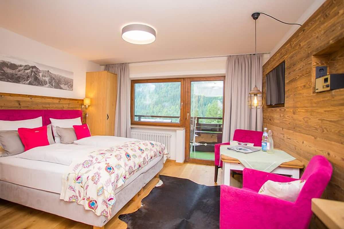 Ein Schlafzimmer mit Bett, Schreibtisch, Stuhl und Blick ins Freie.