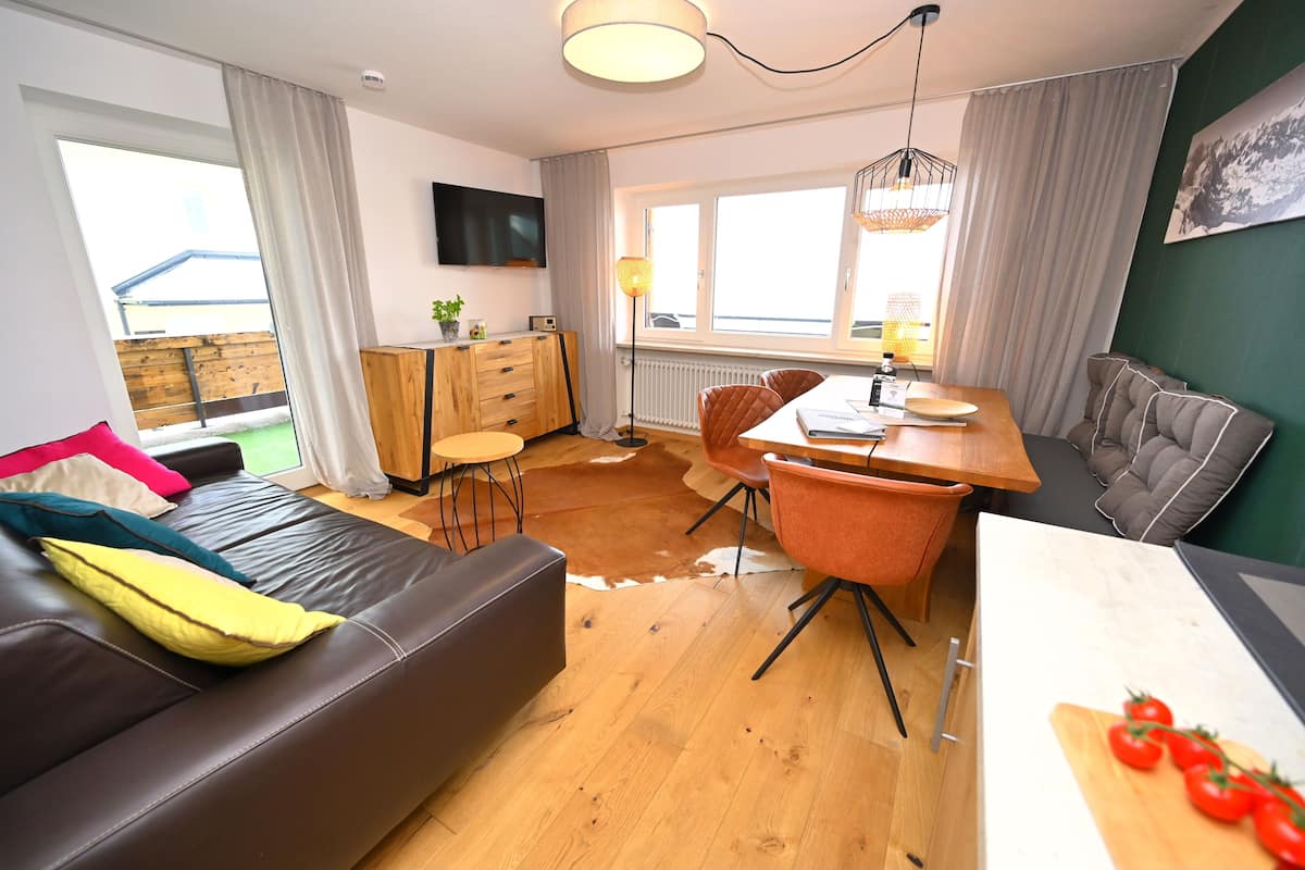 Ein modernes Wohnzimmer mit einer Couch, einem Esstisch, Stühlen und einem an der Wand montierten Fernseher.