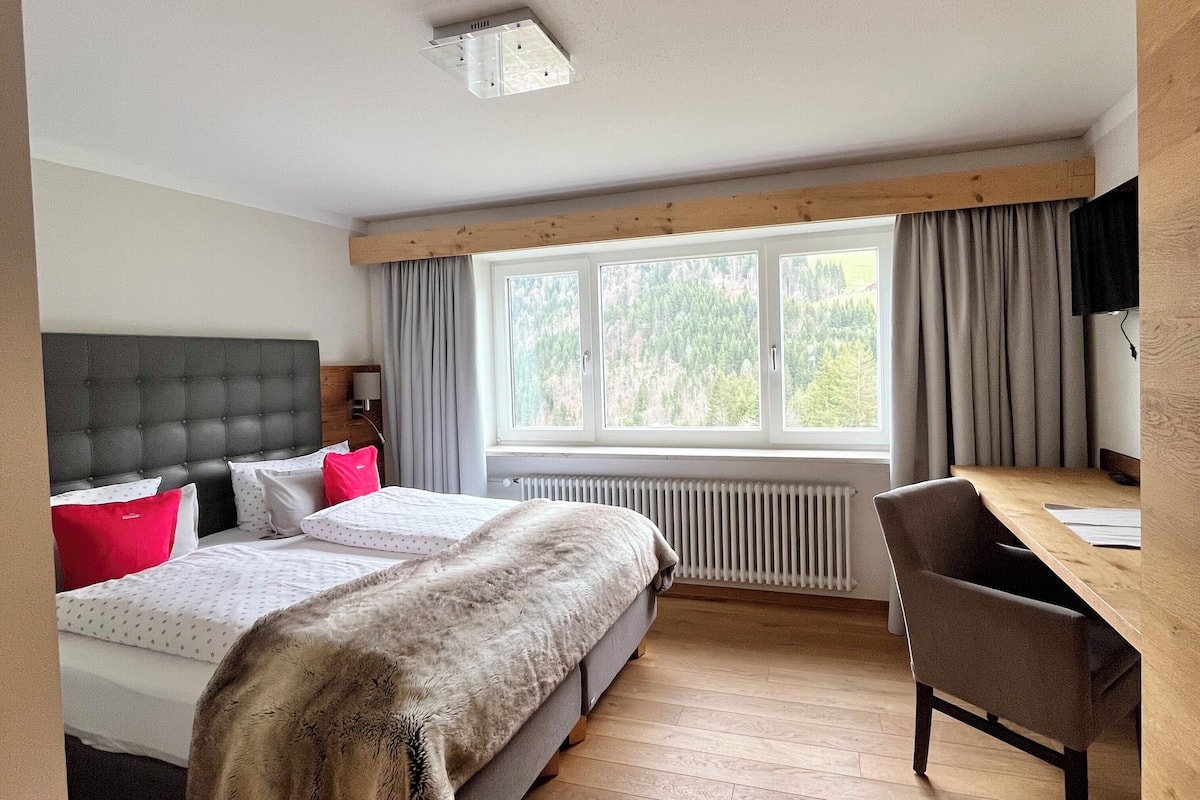 Ein modernes Hotelzimmer mit einem großen Bett, einem Schreibtisch und Blick ins Freie.