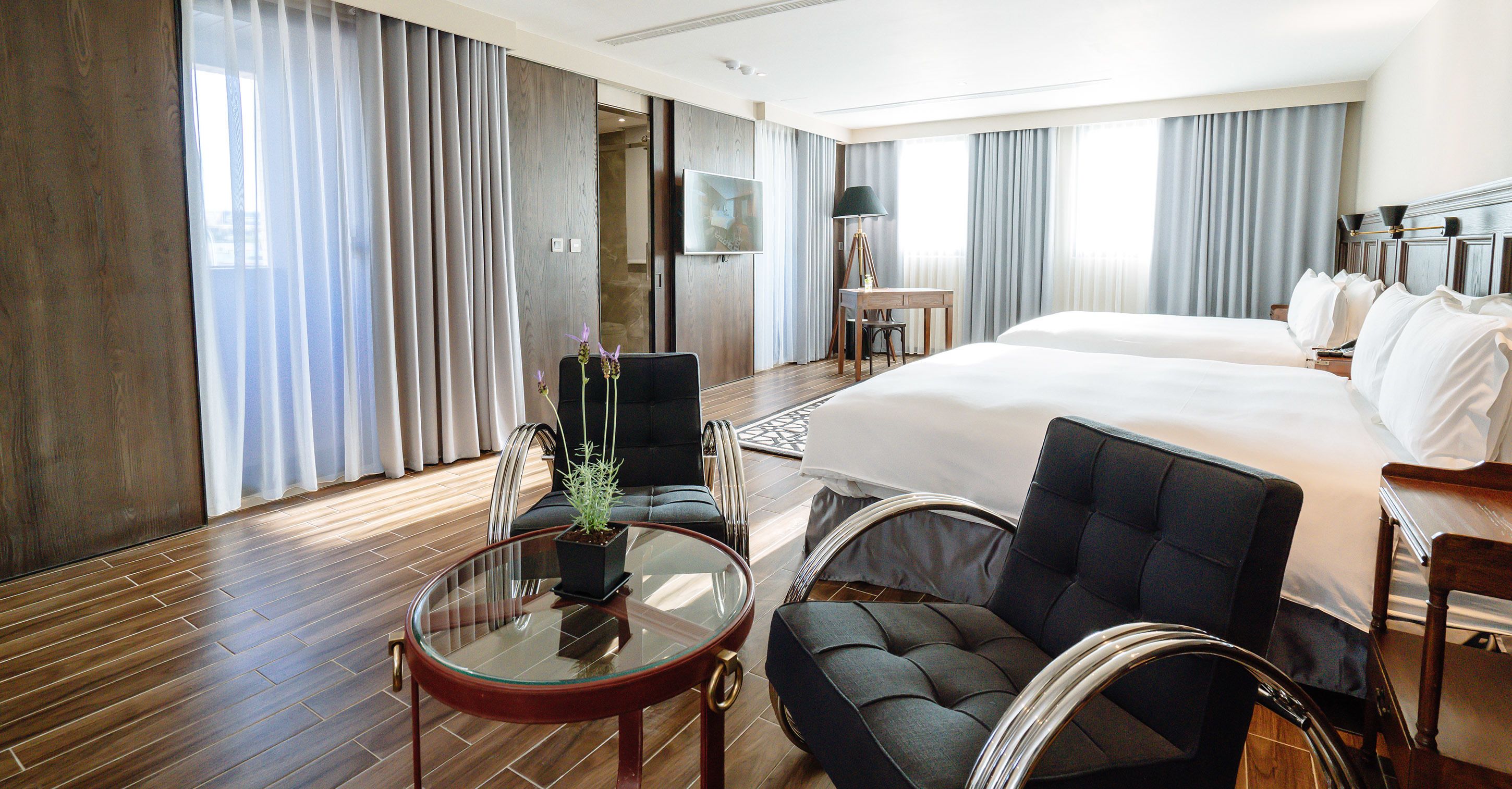 A hotel room with a large bed, a desk, a chair, and a small table with a plant.