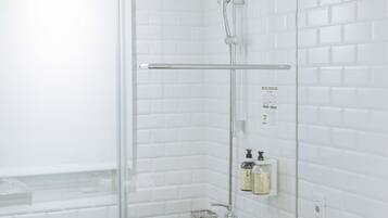 Un baño moderno con azulejos blancos tipo metro, mampara de vidrio, cabezal de ducha manual y dispensador de jabón en la pared.