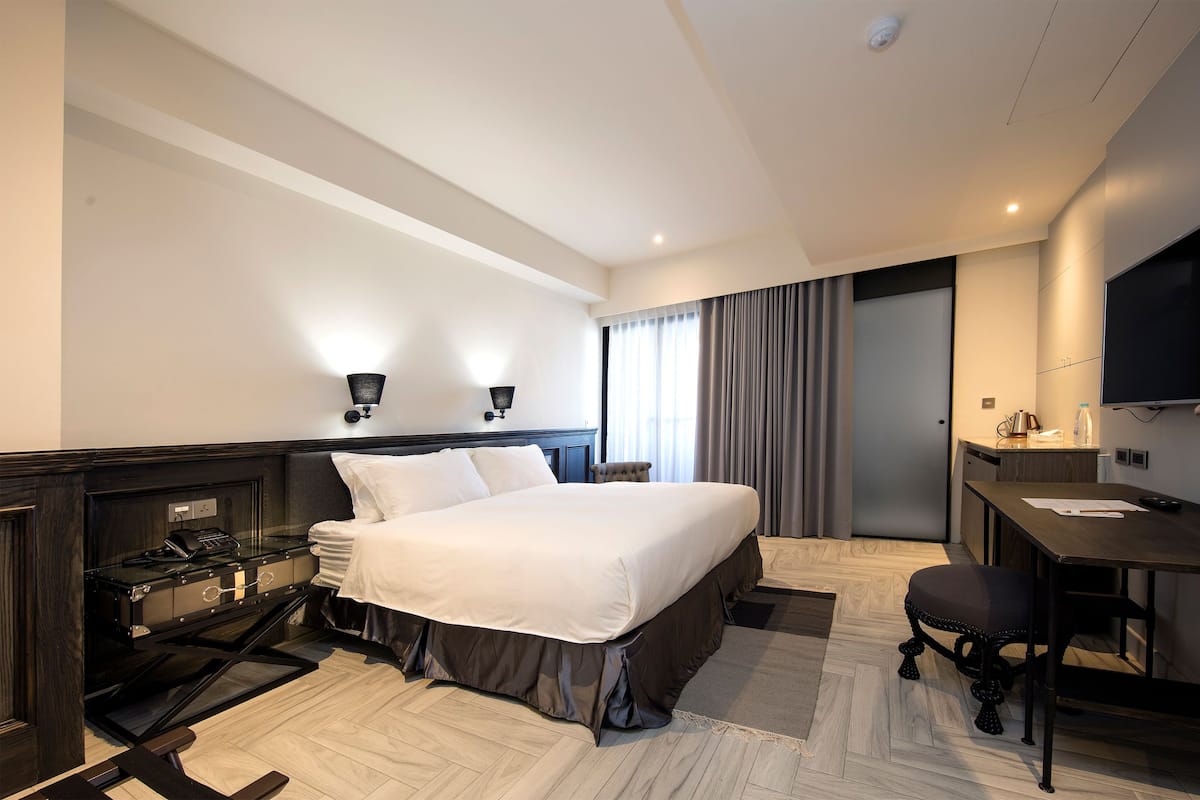 Quarto de hotel com uma cama grande, escrivaninha, cadeira, minibar e televisão.