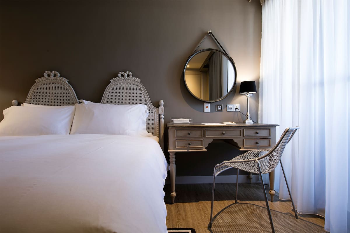 Quarto de hotel com uma cama grande, uma cômoda, uma cadeira e um espelho na parede.