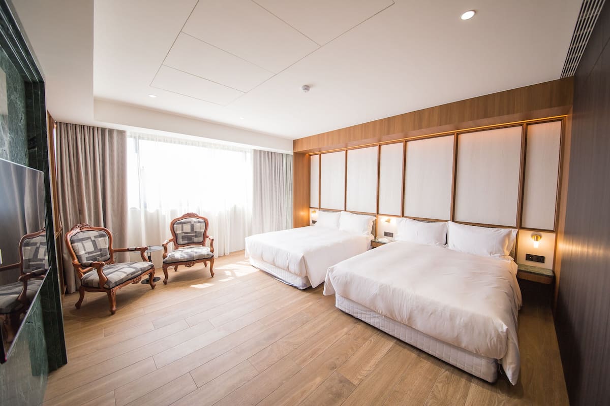 Quarto de hotel com duas camas, piso de madeira, um espelho grande e uma janela com cortinas.
