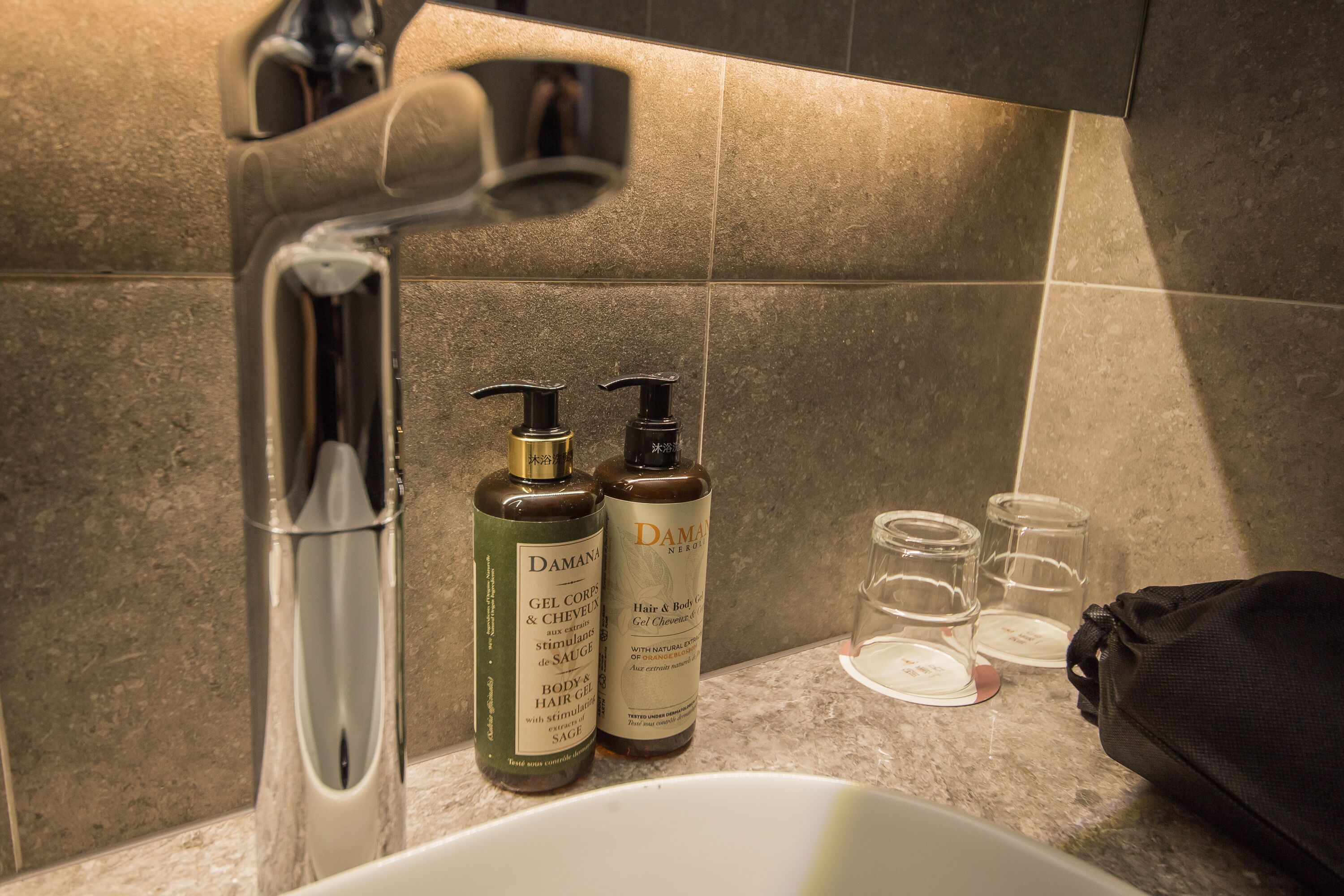 A bathroom with a sink, two bottles of hair care products, and two empty glasses on the counter.