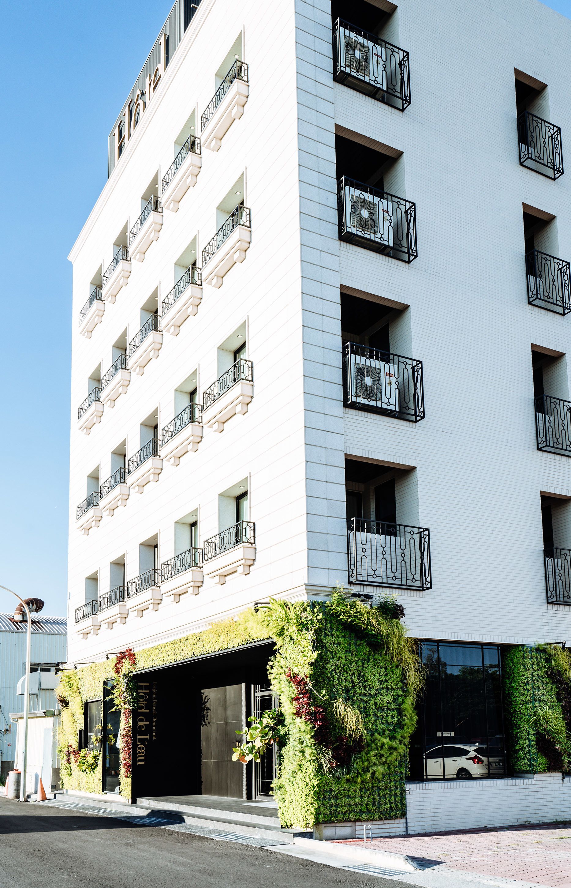 Un hotel de varios pisos con balcones, una entrada cubierta y jardines verticales.