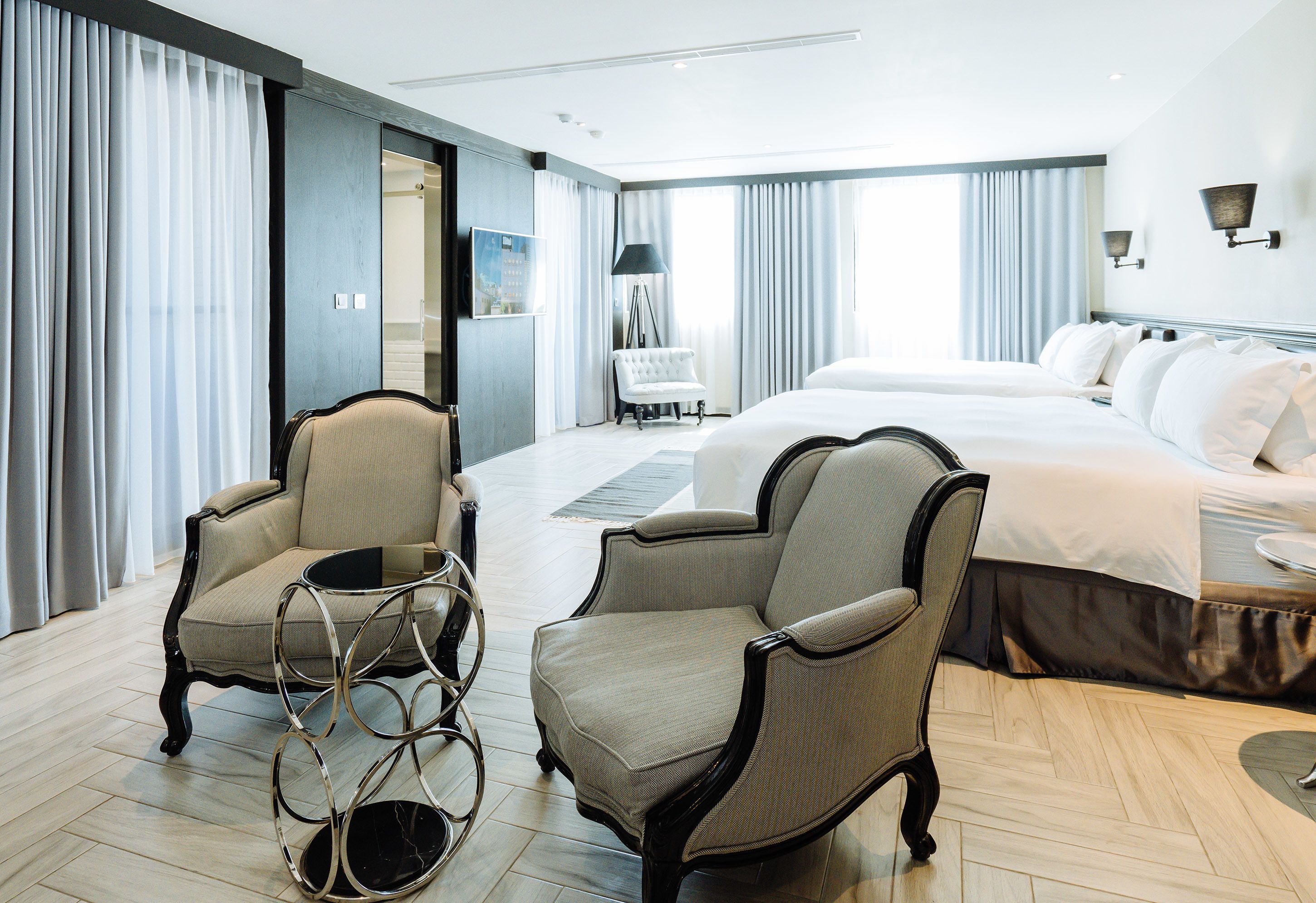 Ein Hotelzimmer mit einem großen Bett, zwei Sesseln, einem Beistelltisch und Blick auf die Stadt.