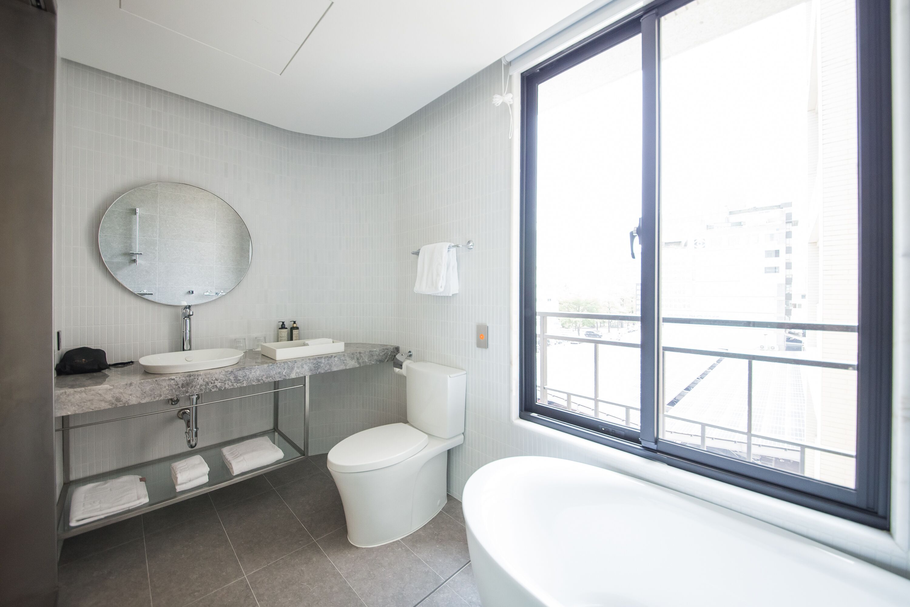 A modern bathroom with a round mirror, a sink, a toilet, and a bathtub.
