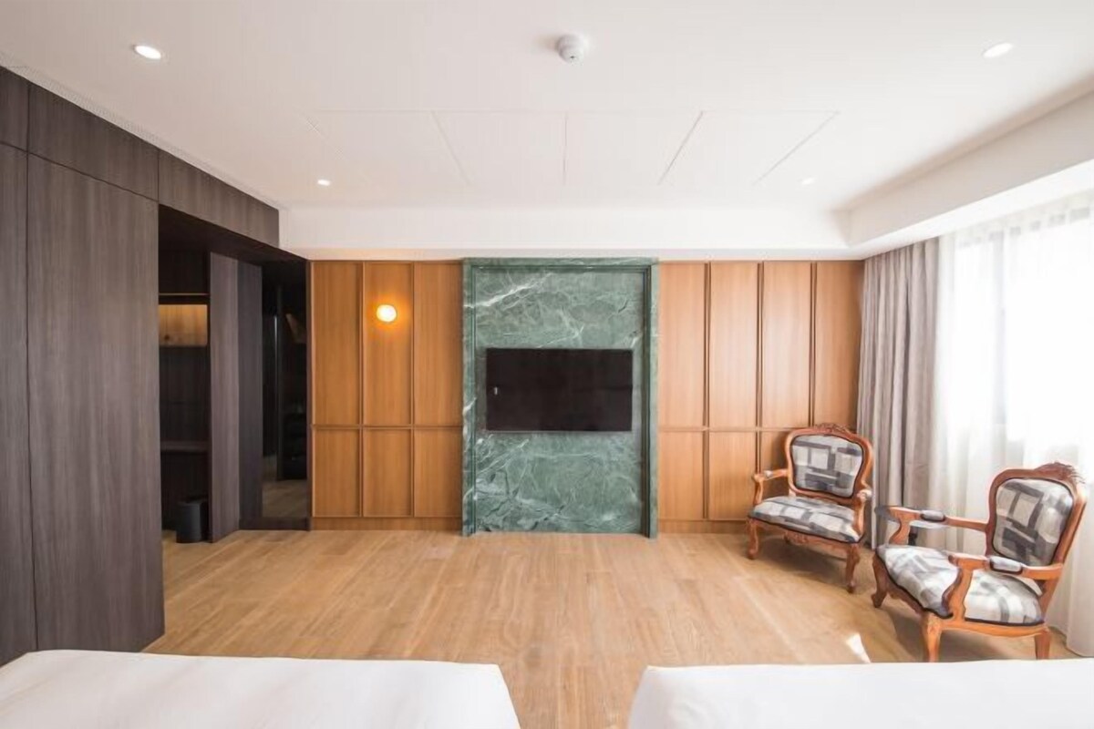 A hotel room with a wooden floor, a green marble fireplace, two wooden chairs, and a flat-screen TV mounted on the wall.