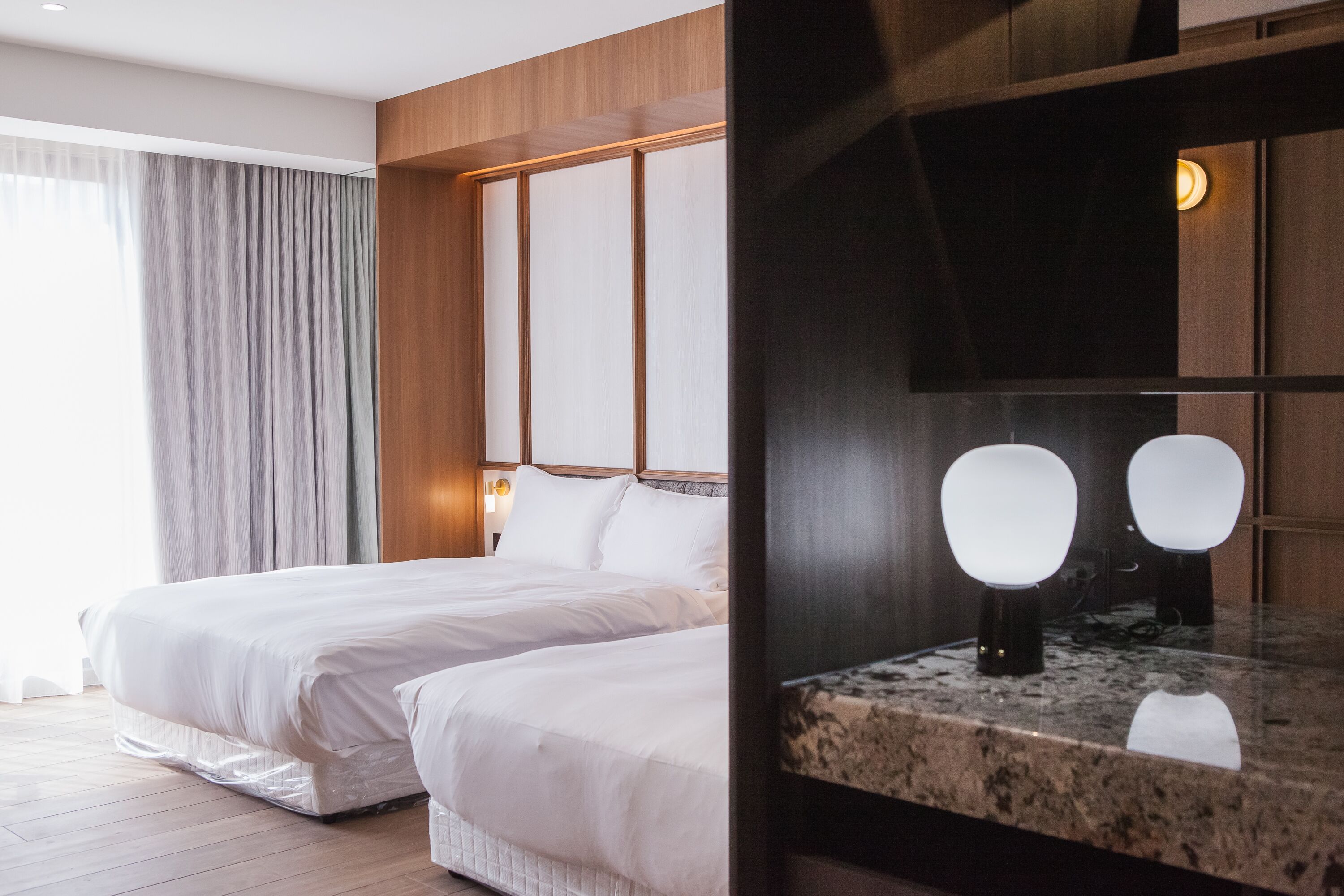 Quarto de hotel com uma cama grande, cabeceira de madeira, bancada de mármore e um espelho.
