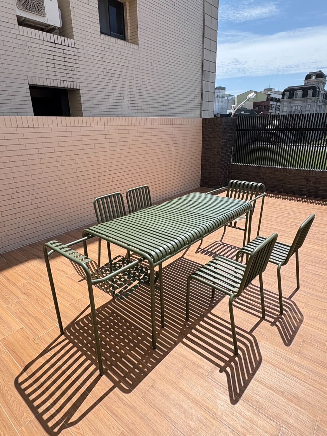 A rooftop patio with a metal table and chairs, a brick wall, and a view of buildings in the background.