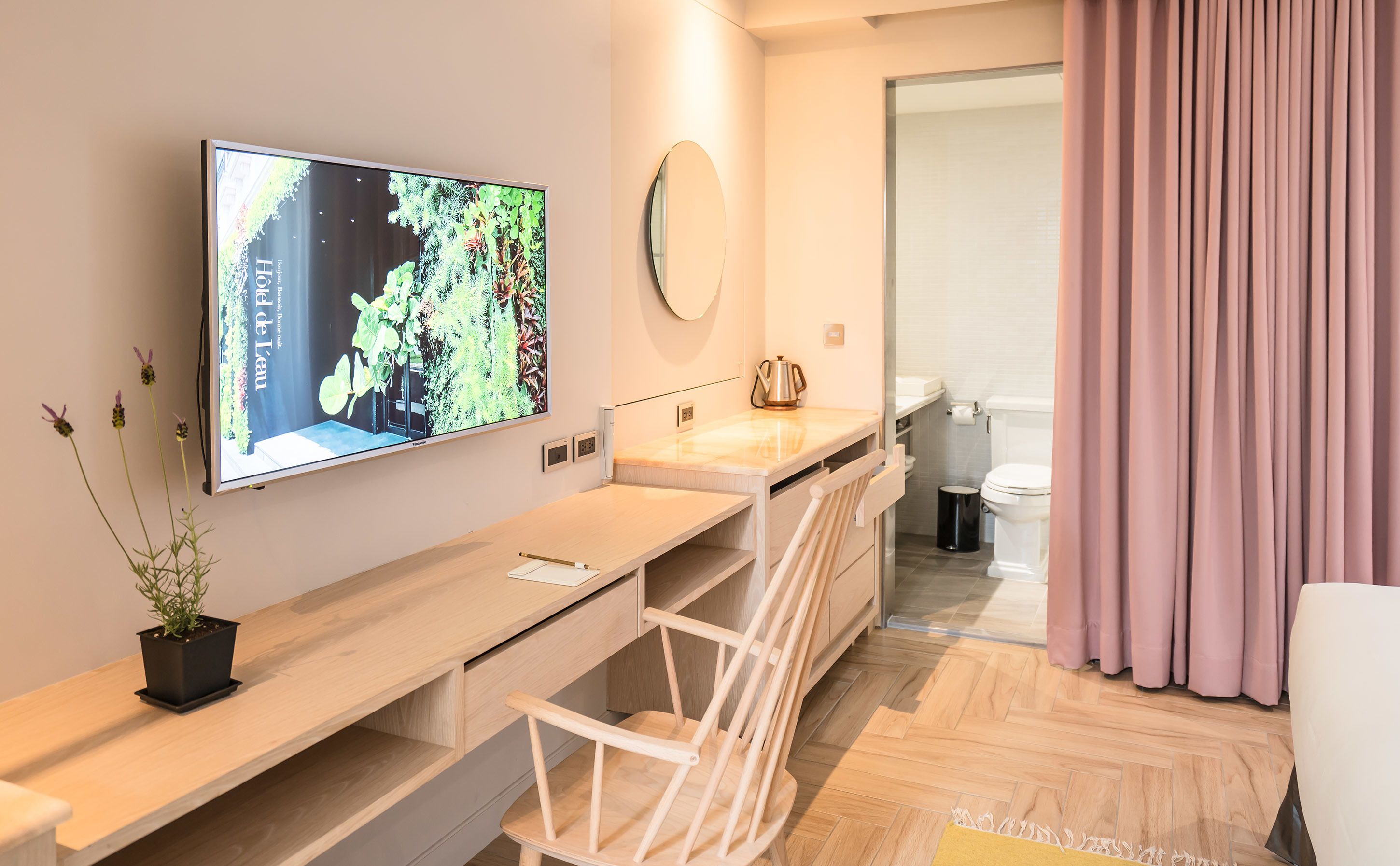 Un baño moderno con tocador de madera, un espejo, una televisión montada en la pared y un inodoro.