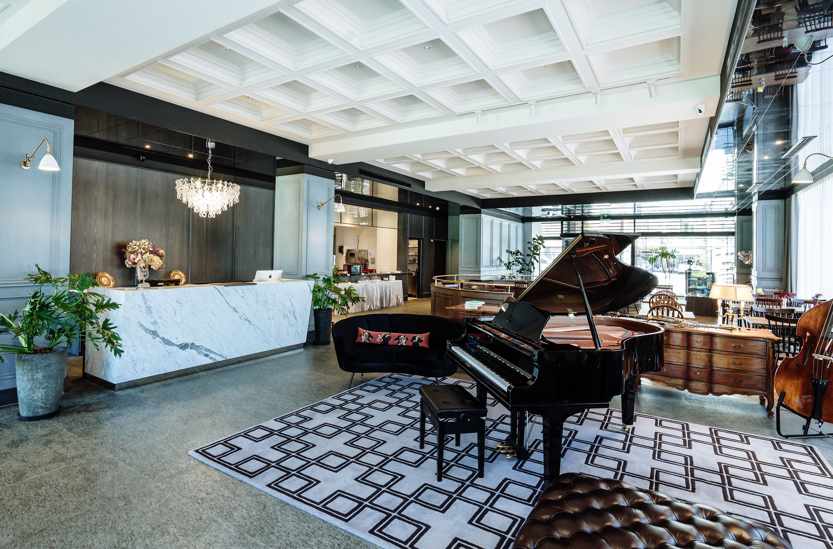 A spacious lobby with a grand piano, a reception desk, and a modern chandelier.