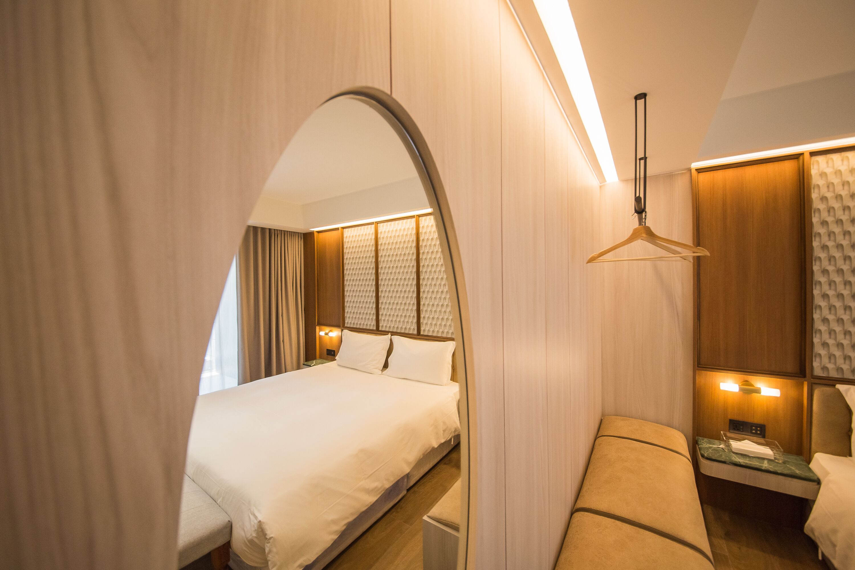 A hotel room with a large bed, a bedside table with a lamp, a hanging light fixture, and a mirror.