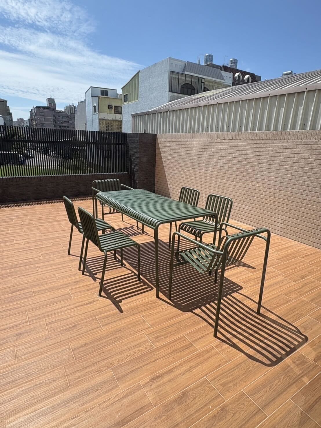 A rooftop patio with a table and chairs, surrounded by a wooden floor and a brick wall.