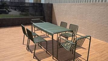 A rooftop patio with a table and chairs, surrounded by a wooden floor and a brick wall.