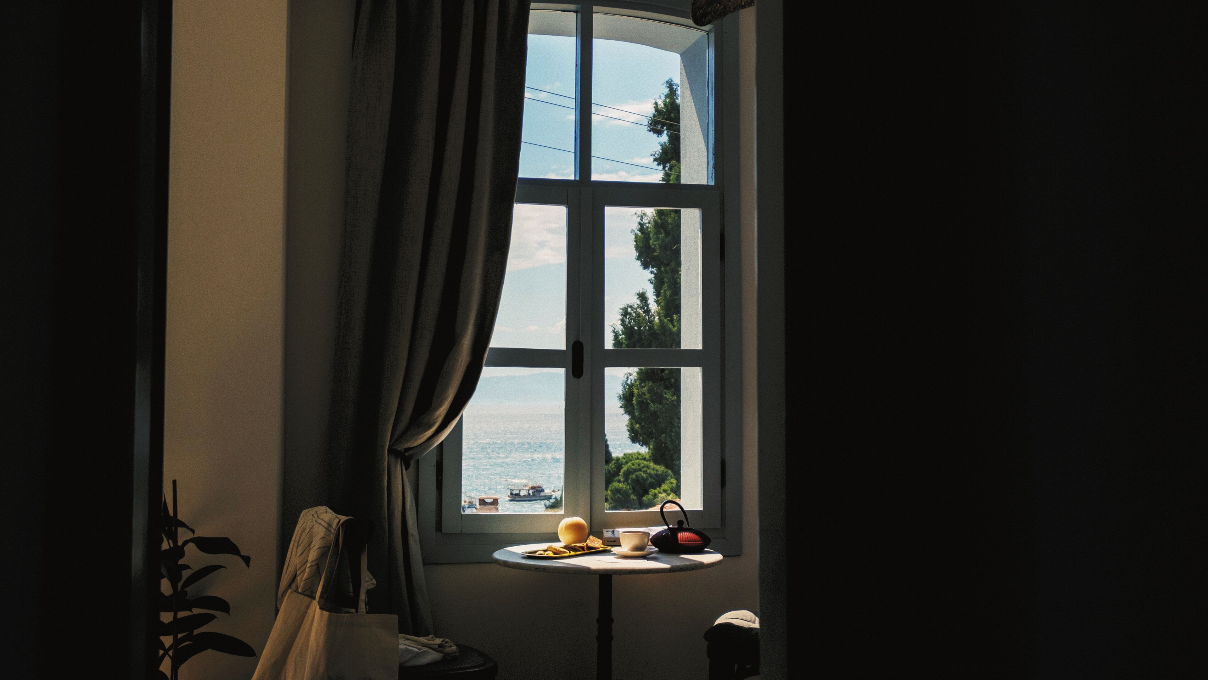 A room with a large window, a small table with a cup, a bowl, and a teapot.