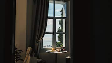 A room with a large window, a small table with a cup, a bowl, and a teapot.