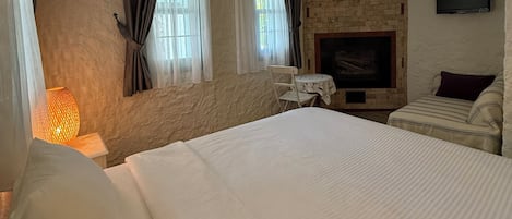 A bedroom with a large bed, a fireplace, a table, and a hanging light fixture.