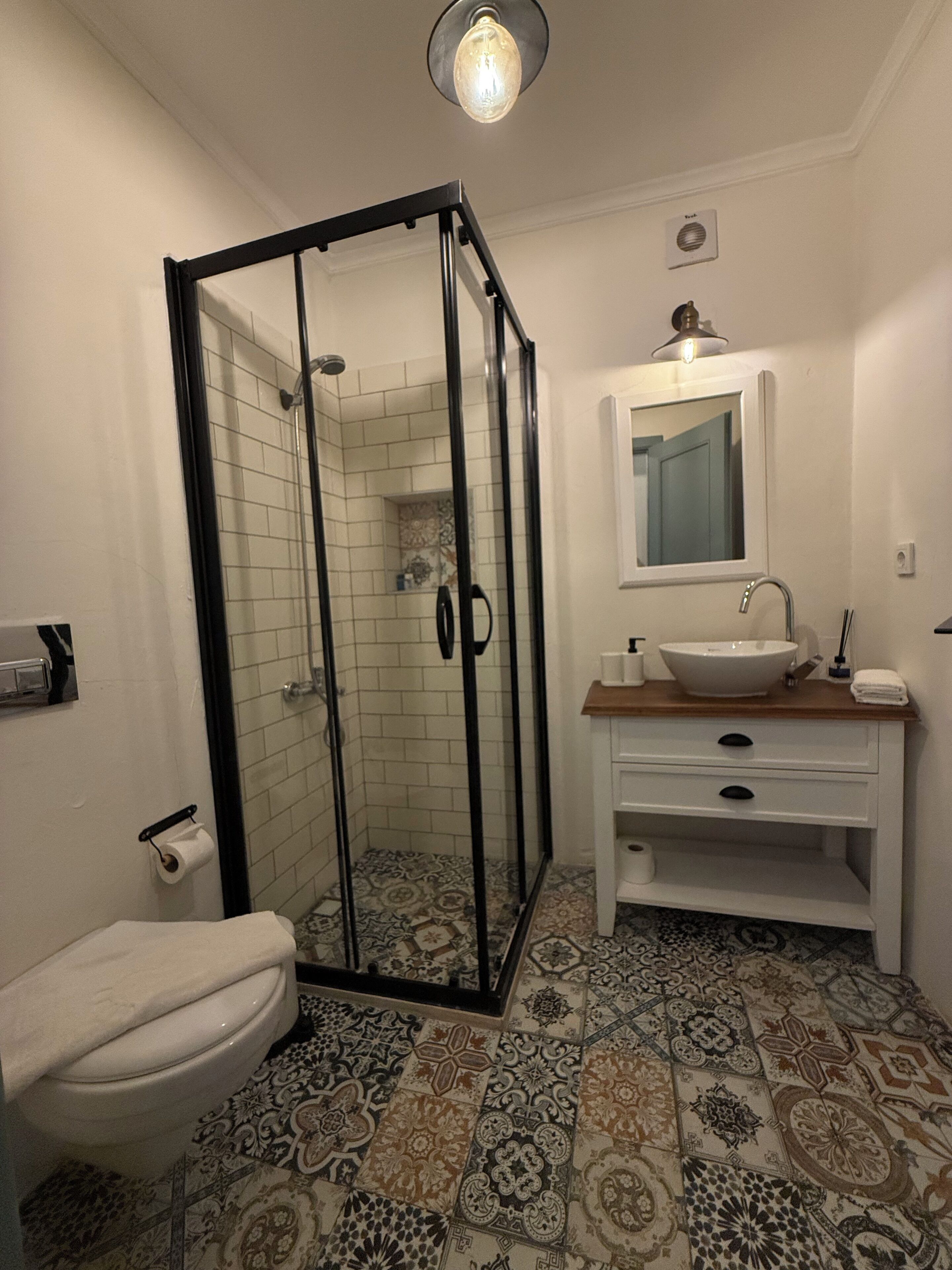 Un baño con ducha de mampara de vidrio, un lavabo blanco y un espejo encima.