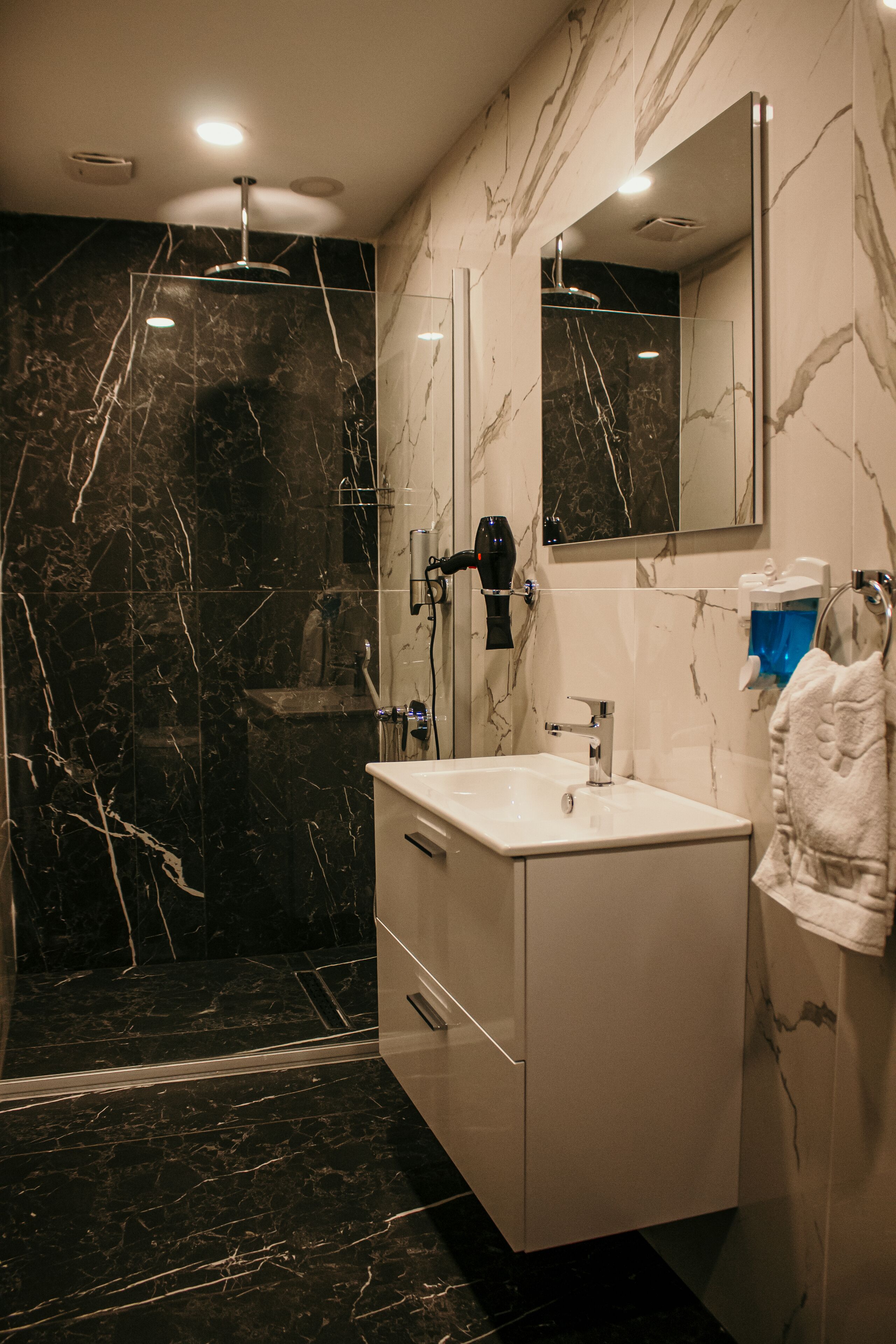 Une salle de bain moderne avec une douche en marbre, un lavabo blanc et un grand miroir.